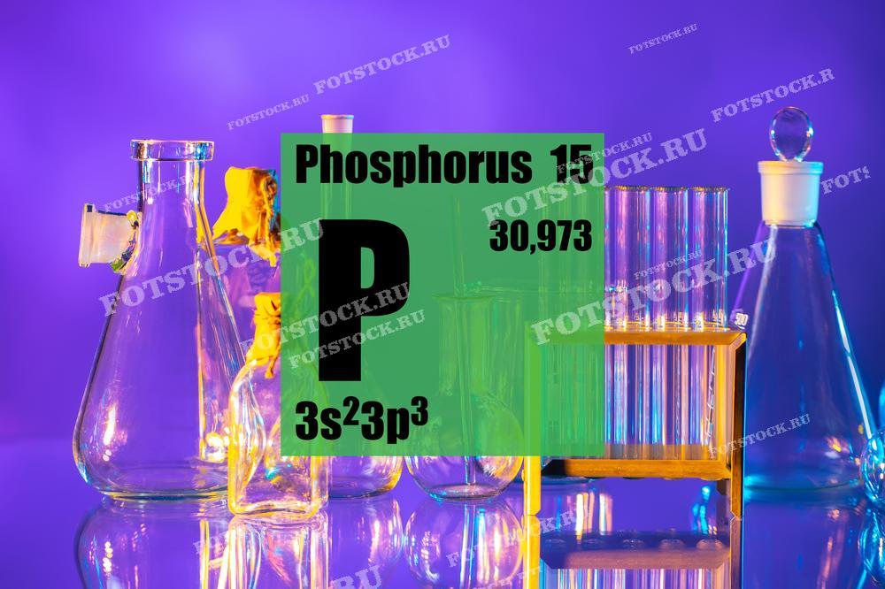 На фотографии изображены надпись "Phosphorus", химическая формула фосфора (3s²3p³) и его атомный номер 15 на зеленом фоне. На заднем плане видны лабораторные колбы и пробирки, создающие атмосферу научных исследований в лаборатории.